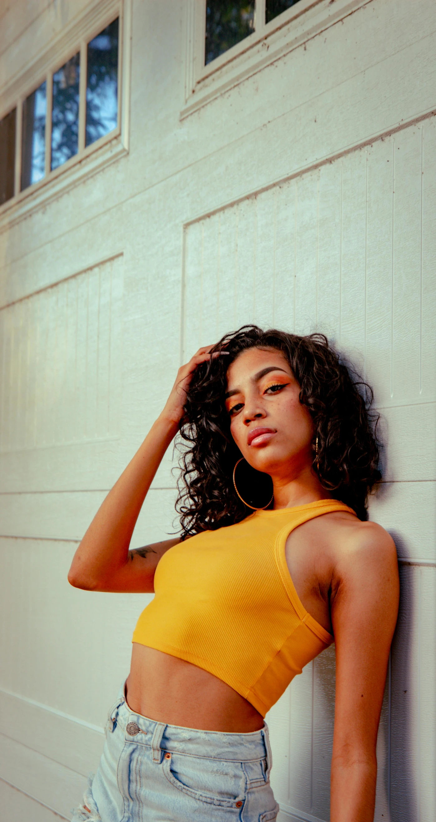 a woman leaning against a garage door, inspired by Elsa Bleda, trending on pexels, wearing yellow croptop, portrait of vanessa morgan, ashteroth, digital image