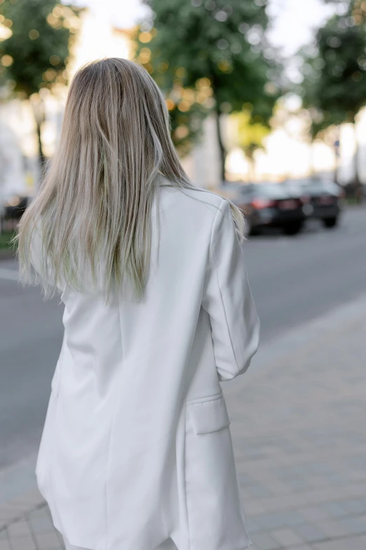 a woman in white is walking down the street, trending on pexels, soft hair. light color palate, facing away, silver highlights, wearing a blazer