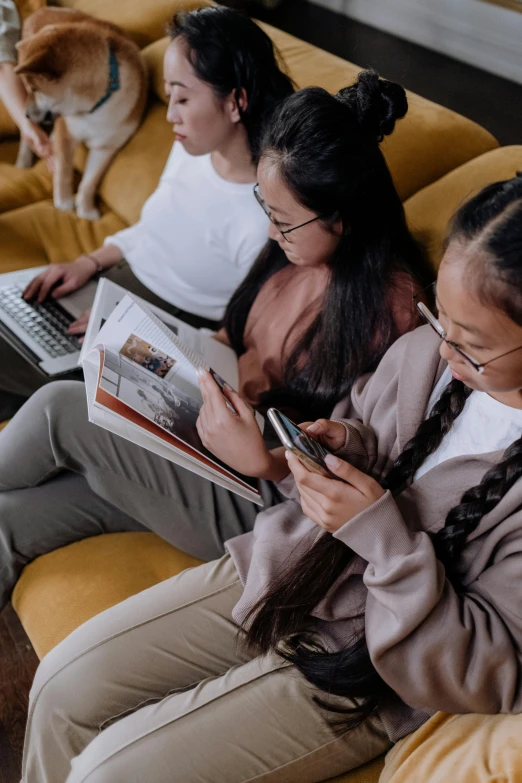 a group of women sitting on top of a yellow couch, a picture, trending on pexels, reading a newspaper, young asian girl, mobile learning app prototype, two buddies sitting in a room