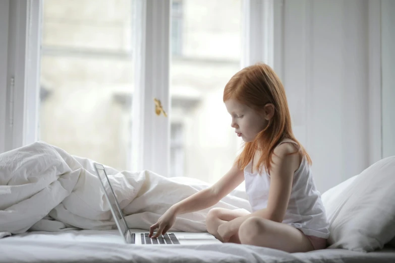 a little girl sitting on a bed with a laptop, pexels contest winner, hr ginger, programming, white hue, 1 2 9 7