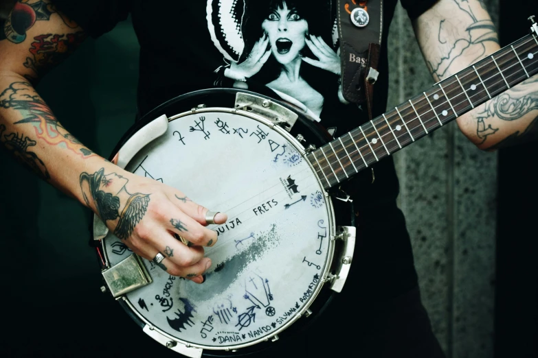 a close up of a person holding a banjo, pexels contest winner, graffiti, band merchandise, inking on skin, jean deville, circle pit