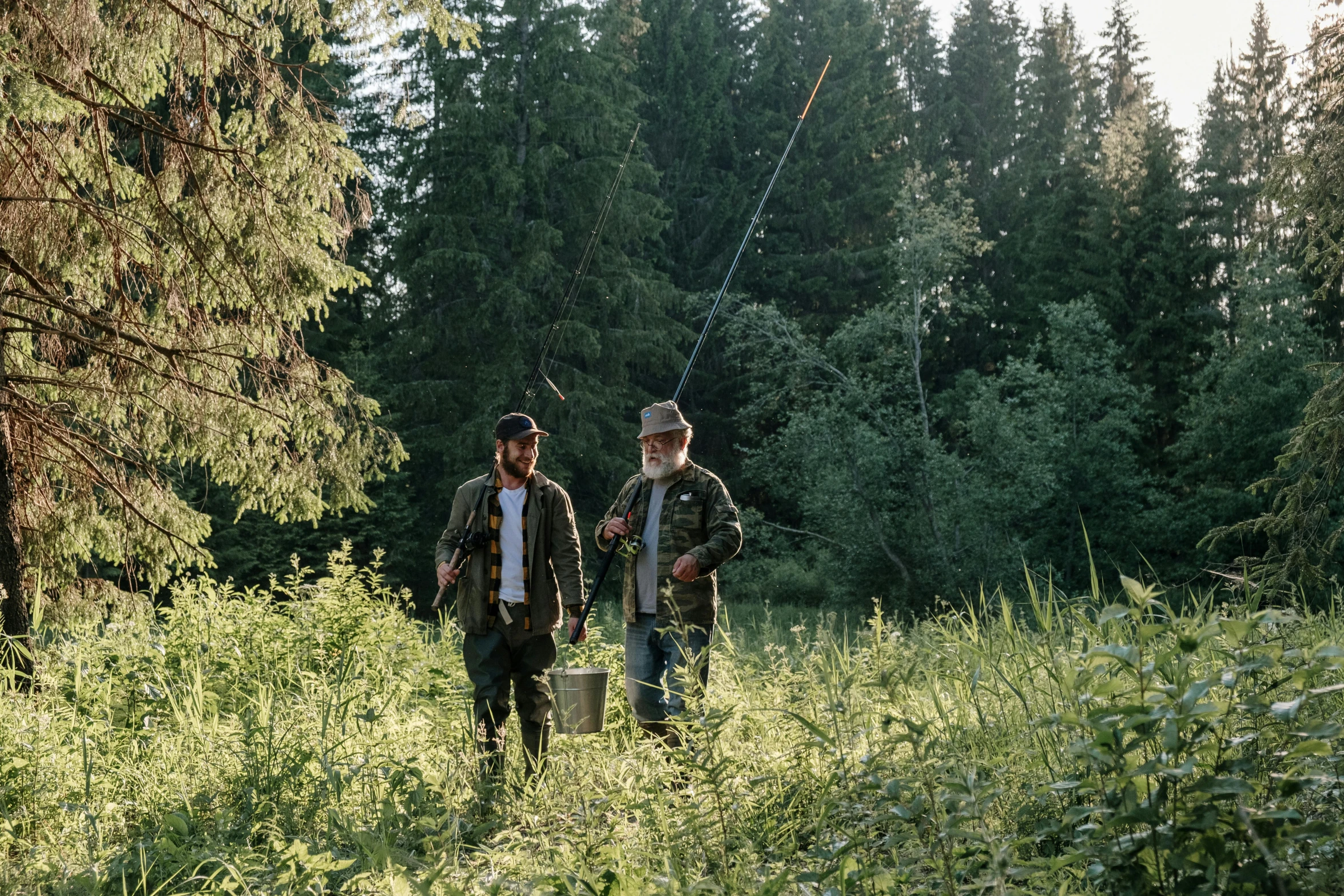 a couple of men standing on top of a lush green field, a photo, by Jesper Knudsen, hurufiyya, fishing, forest picnic, production still, first light