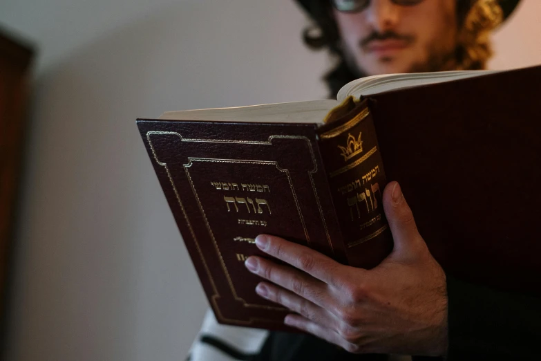 a man holding a book in his hands, an album cover, by Daniel Lieske, pexels, unilalianism, hebrew, an intricate, religious, photographed for reuters