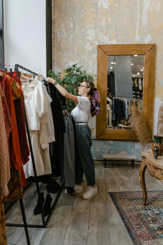 a woman standing in front of a rack of clothes, looking in a mirror, sustainable materials, storefronts, inspect in inventory image