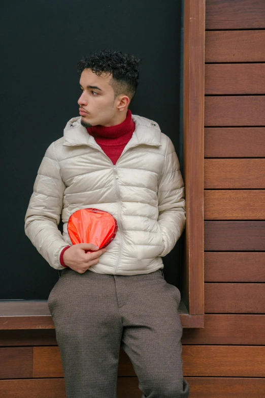 a man sitting on a window sill in front of a blackboard, an album cover, inspired by Mario Bardi, pexels contest winner, renaissance, model wears a puffer jacket, red orange blue beige, holding a gold bag, white puffy outfit