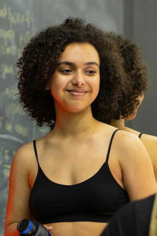 a woman standing in front of a blackboard with writing on it, curly hair, wearing leotard, acting headshot, teenager girl