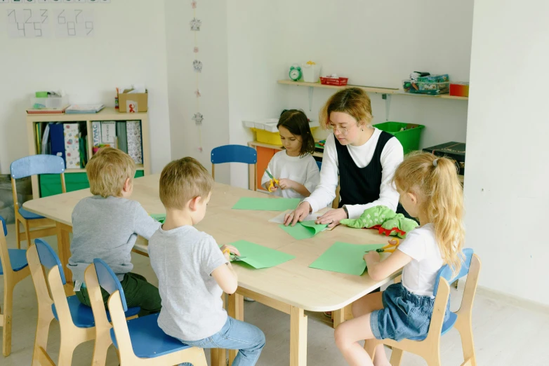 a group of children sitting around a wooden table, sitting at a desk, jovana rikalo, cardboard, teacher