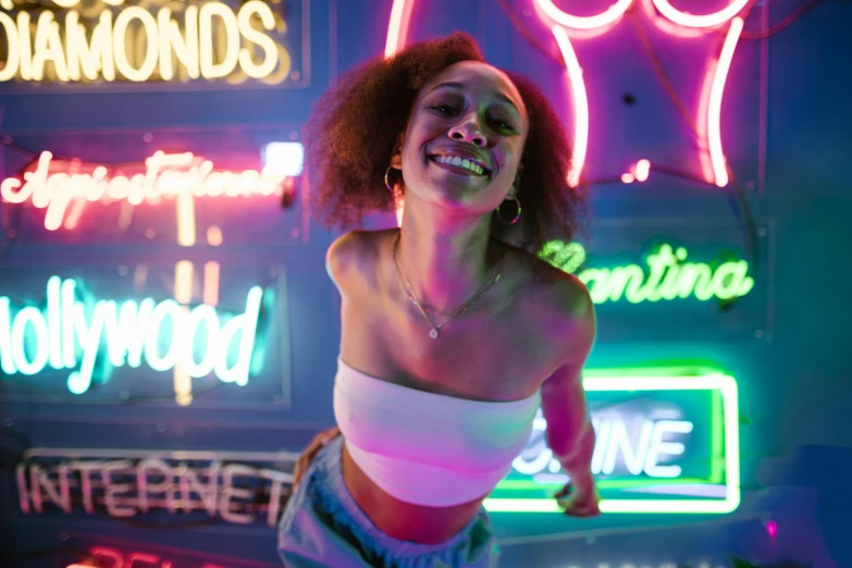 a woman standing in front of neon signs, pexels contest winner, doja cat, smiling down from above, natural lighting, laughing