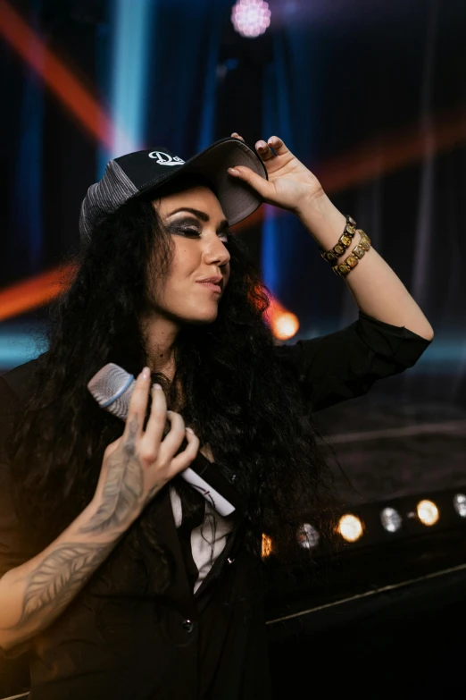 a woman that is holding a microphone in her hand, a tattoo, long curly black hair, 2019 trending photo, moleksandra shchaslyva, wears a destroyed hat