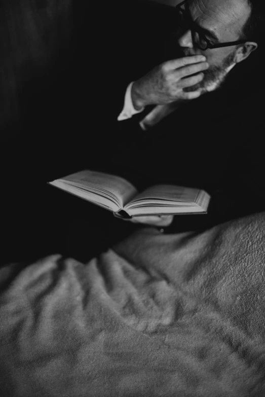 a black and white photo of a man reading a book, a black and white photo, inspired by Louis Stettner, unsplash, conceptual art, bed, holding grimoire, gentleman, hands