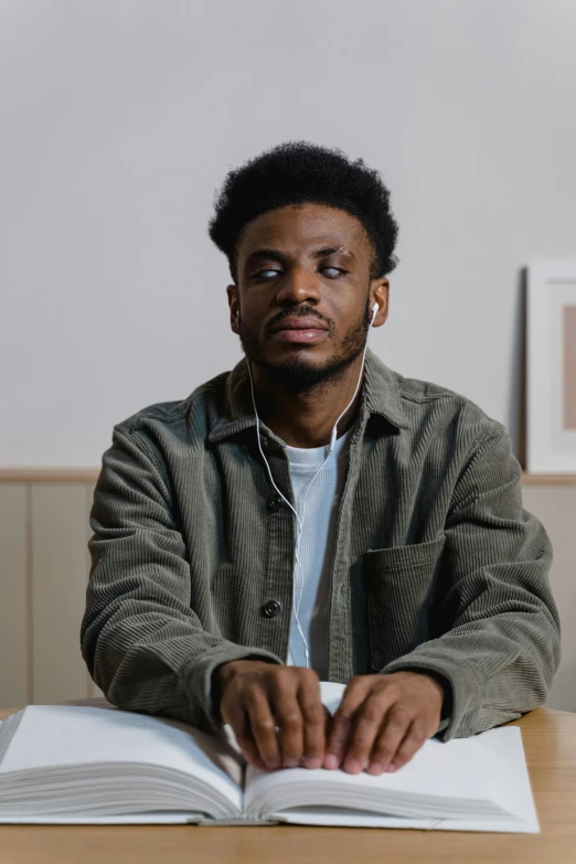 a man sitting at a table with an open book, an album cover, inspired by Xanthus Russell Smith, trending on pexels, realism, proud looking away, worried, jaylen brown, neutral focused gaze