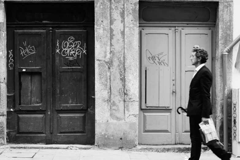 a black and white photo of a man walking down the street, by Emma Andijewska, pexels contest winner, minimalism, leaning on door, traditional corsican, contrasting colours, business men