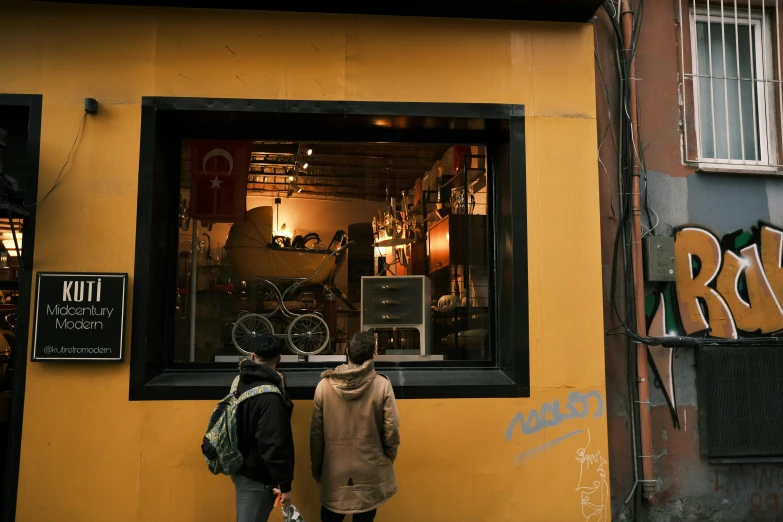 a couple of people that are standing in front of a building, a photo, shopwindows, mustard, istanbul, facing away from the camera