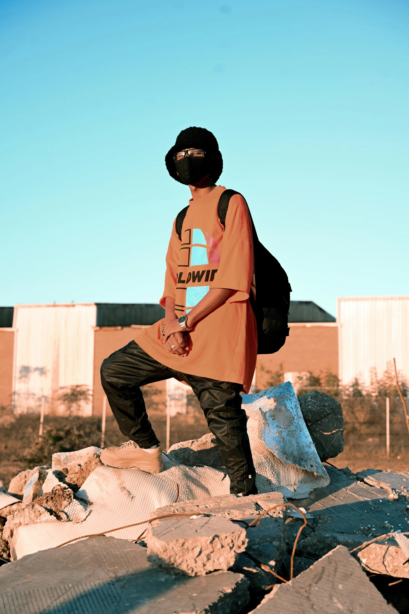 a man standing on top of a pile of rubble, unsplash, graffiti, orange balaclava, baggy clothing and hat, lil uzi vert, ( ( theatrical ) )