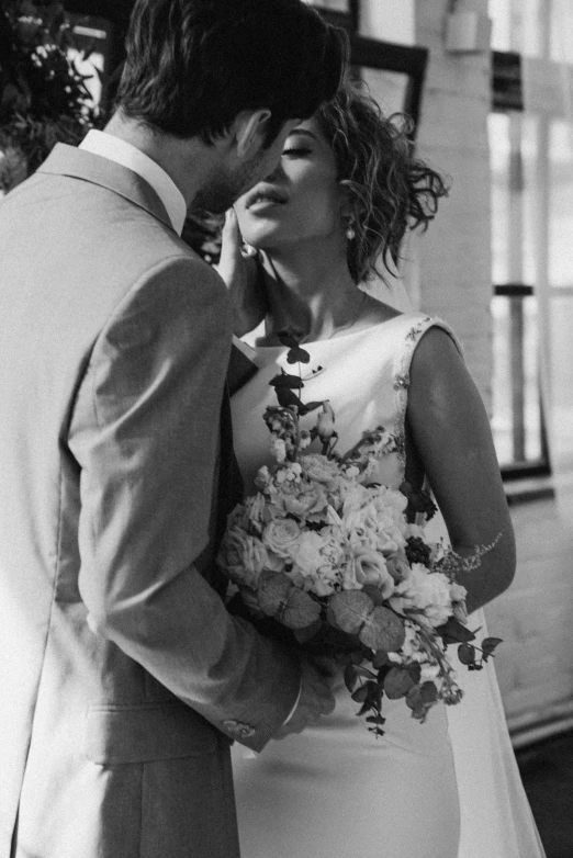 a black and white photo of a bride and groom, by Anita Malfatti, bouquet, hand on cheek, instagram picture, head bowed slightly