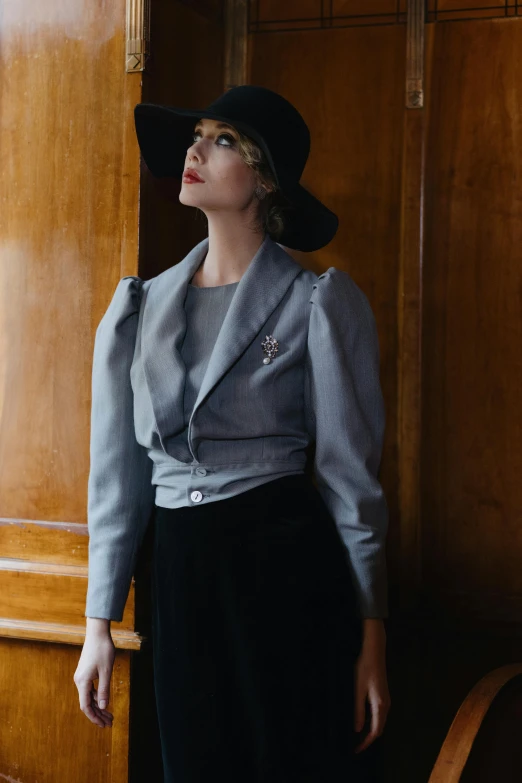 a woman in a hat leaning against a wall, a portrait, inspired by Vint Lawrence, unsplash, renaissance, grey suit, cropped shirt with jacket, haute couture fashion shoot, circa 1940s