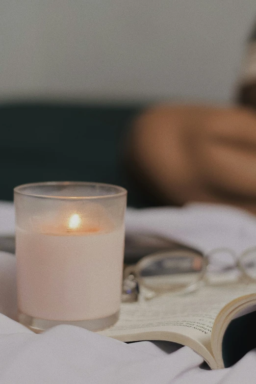 an open book sitting on top of a bed next to a candle, light pink mist, dynamic closeup, ignant, college