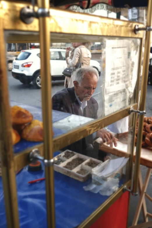 a man standing in front of a display case filled with donuts, tel aviv street, old man doing hard work, bun ), trending photo