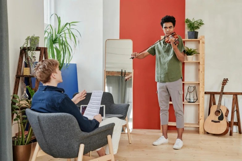 a man playing a violin in a living room, pexels contest winner, standing in class, two buddies sitting in a room, cardboard cutout, promotional image