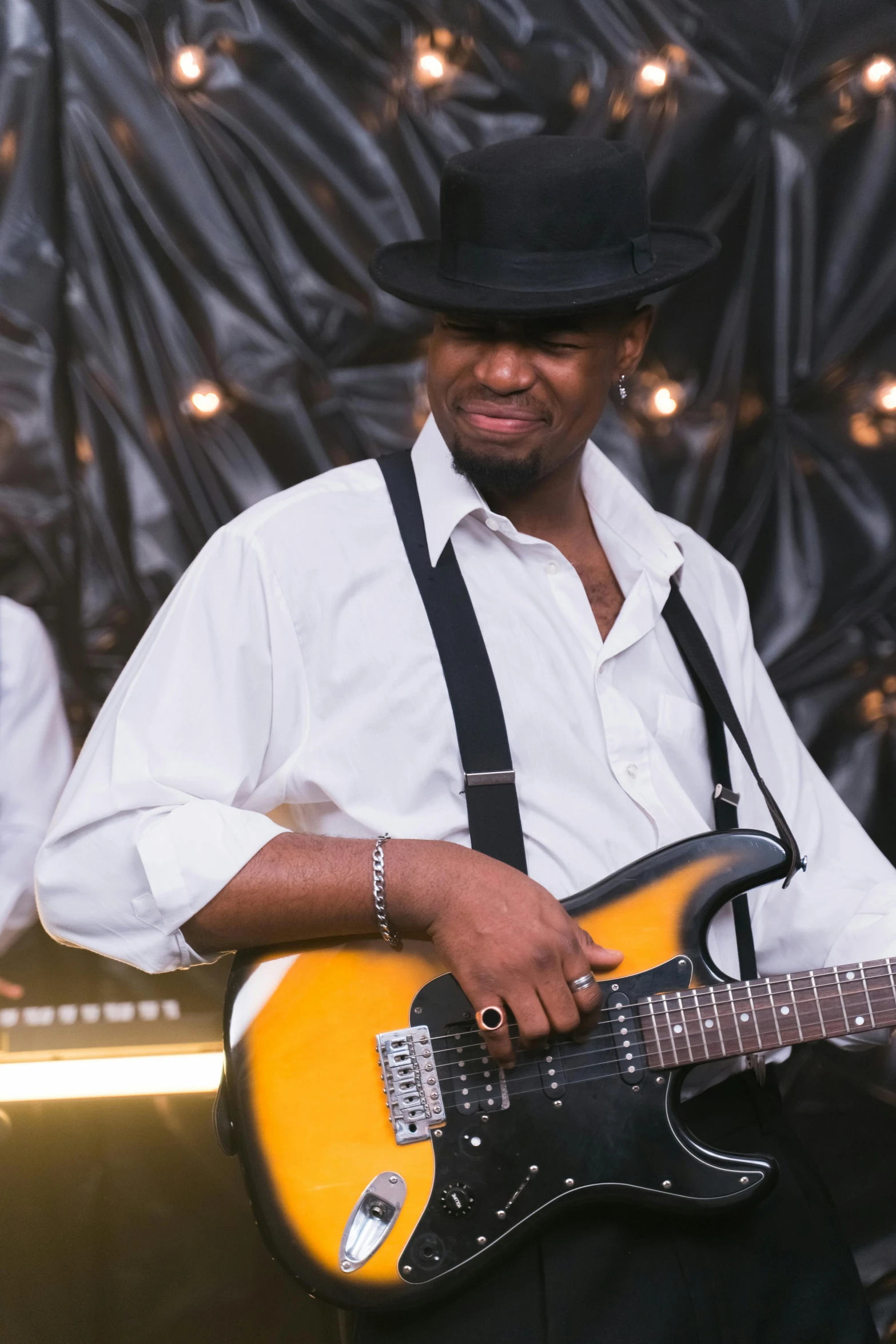 a man that is standing up with a guitar, tipping his fedora, jemal shabazz, slightly smirking, guitarists