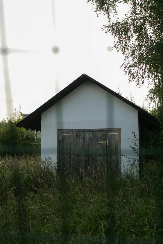 a small white building sitting in the middle of a field, inspired by Isaac Levitan, flickr, graffiti, witch hut, [ 4 k photorealism ], very sparse detail, a ghetto in germany