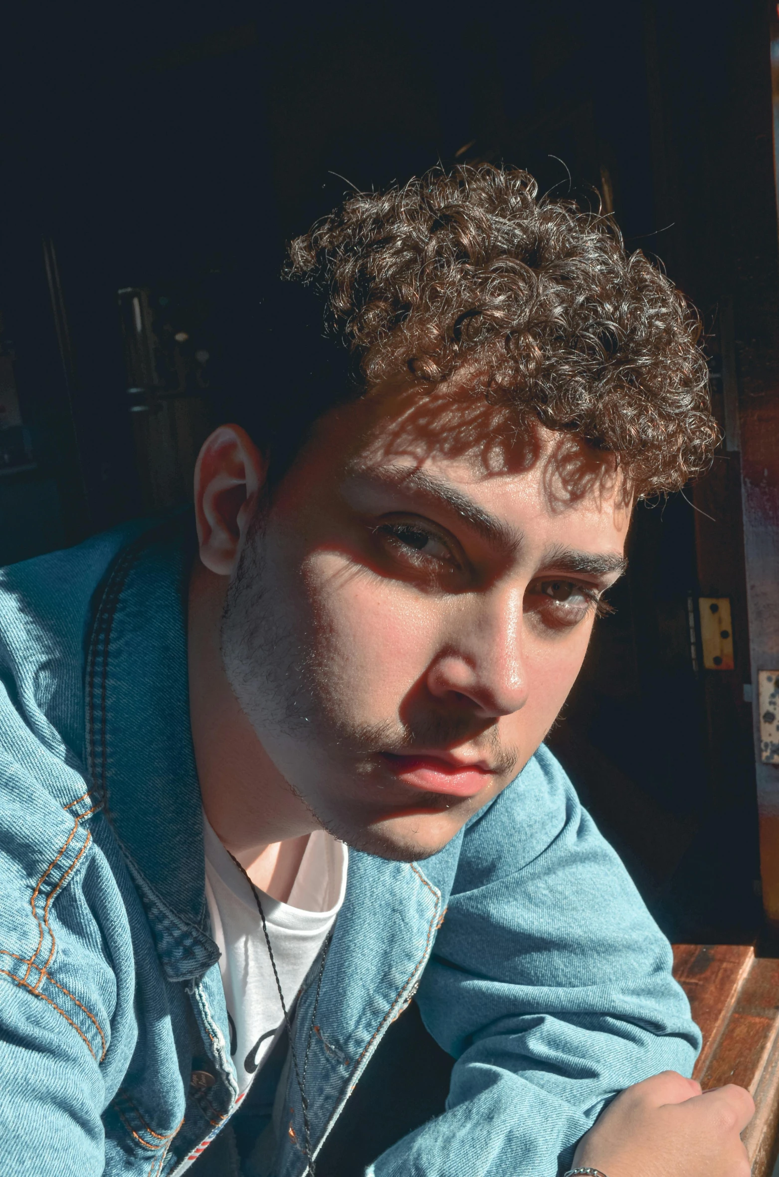 a man sitting at a table with a plate of food, an album cover, by Robbie Trevino, trending on pexels, photorealism, curly bangs, beautiful young man, gal yosef, portrait close up of guy