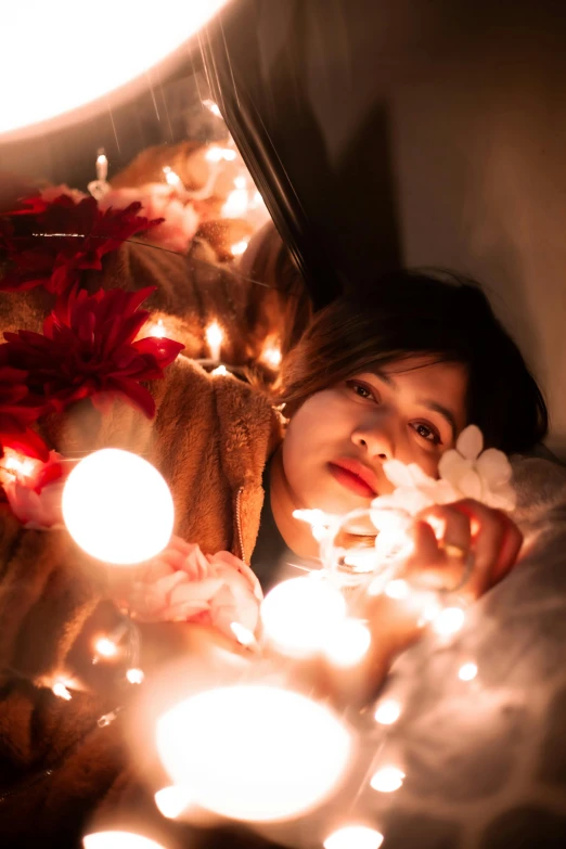 a woman laying on top of a bed covered in christmas lights, inspired by Elsa Bleda, pexels contest winner, asian girl, reflecting, gif, flowers