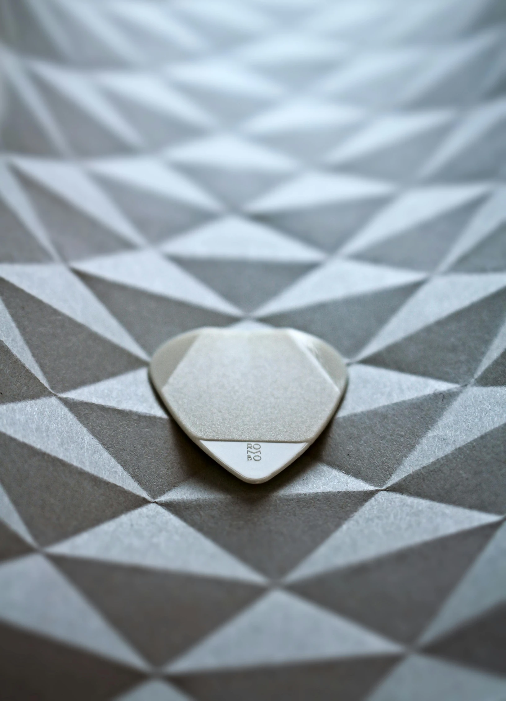 a guitar pick sitting on top of a table, by Adam Marczyński, minimalism, silver，ivory, light sensor, 9 9 designs, solid grey