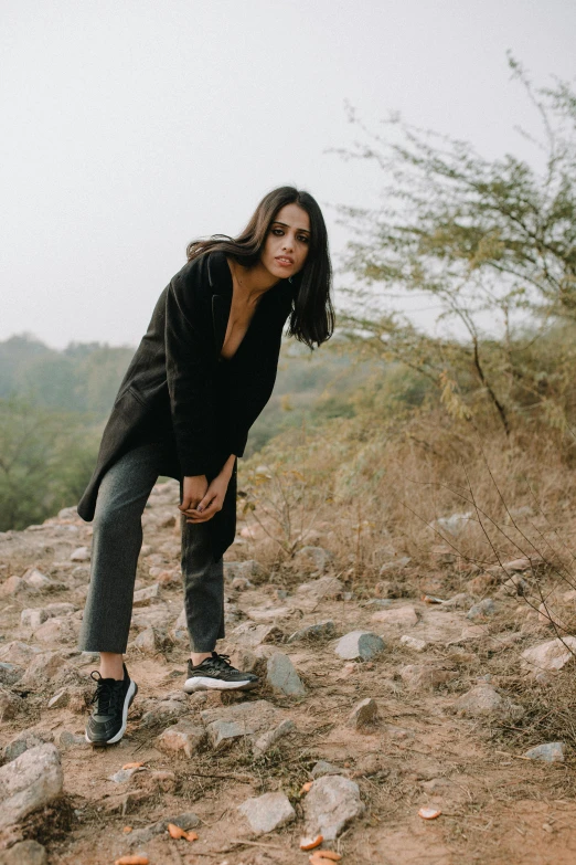 a woman standing on top of a rocky hill, a picture, trending on pexels, black loafers, black haired girl wearing hoodie, provocative indian, fullbody photo