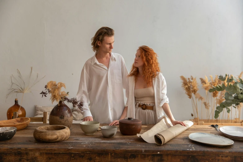 a man and a woman standing in front of a table, by Emma Andijewska, pexels contest winner, renaissance, organic ceramic white, flowing ginger hair, linen, rustic