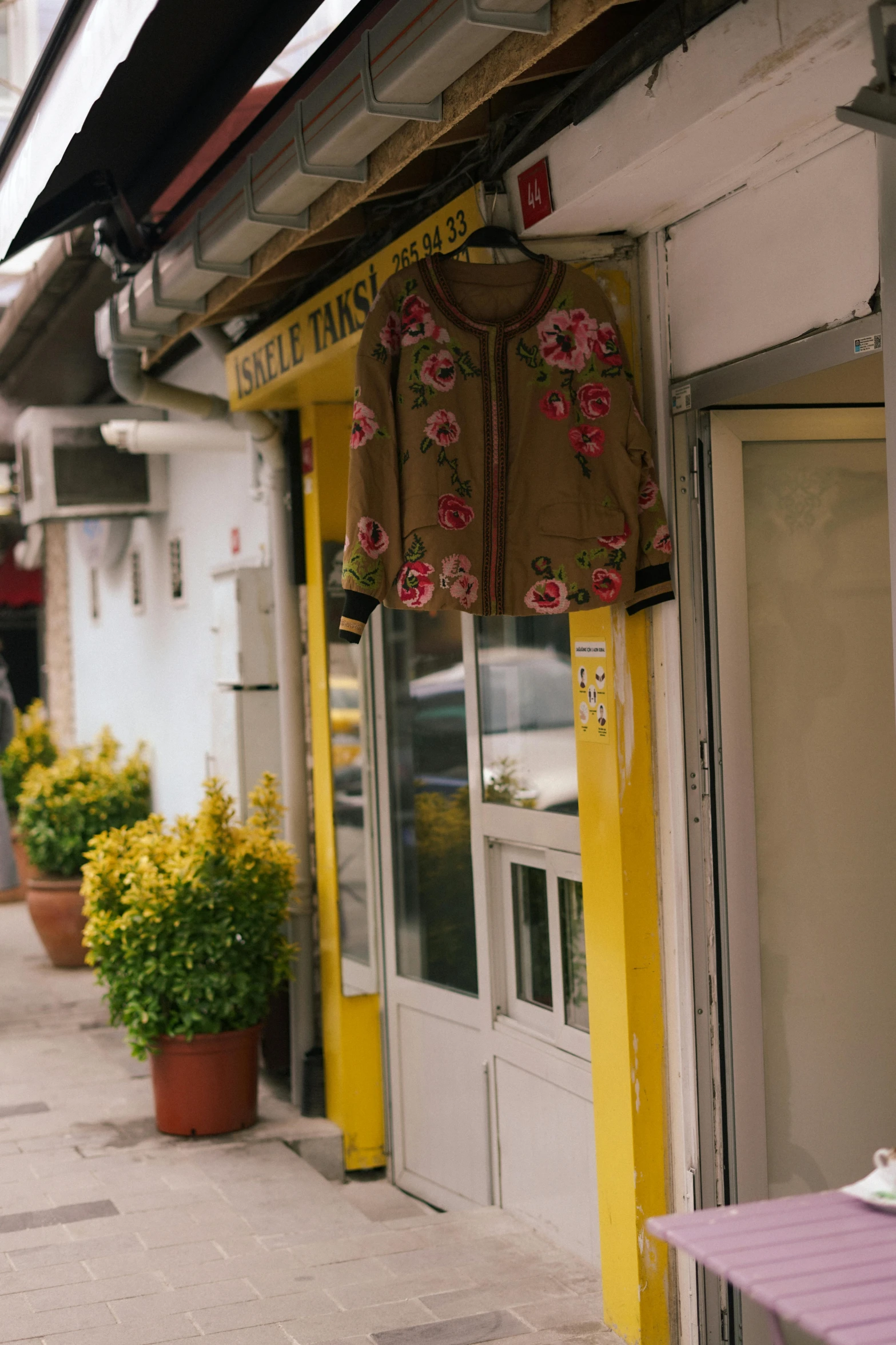 a woman walking down a sidewalk in front of a store, a silk screen, by Matteo Pérez, trending on unsplash, yellow flowers, embroidered robes, quaint village, restaurant