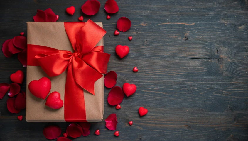 a gift wrapped in brown paper with a red bow surrounded by red rose petals, by Valentine Hugo, pexels contest winner, slide show, a wooden, background image, snacks