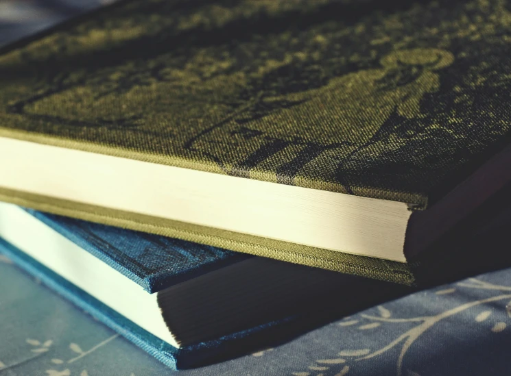 a stack of books sitting on top of a bed, dark blue and green tones, vintage colours, medium shot of two characters, detailed photograph