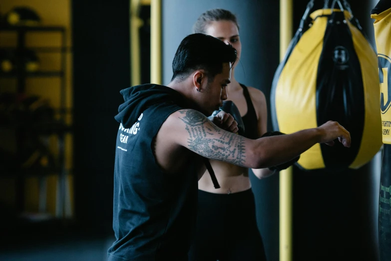 a man standing next to a punching bag, by Tom Bonson, pexels contest winner, hurufiyya, black and yellow tracksuit, male and female, lachlan bailey, hoang lap