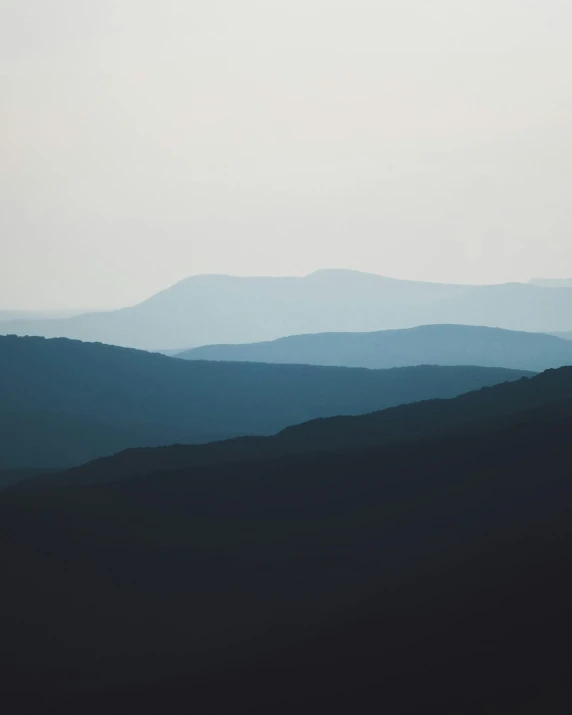 a view of the mountains from the top of a hill, by Attila Meszlenyi, trending on unsplash, minimalism, 3 layers of sky above each other, shades of blue and grey, muted dark colors, silhouette