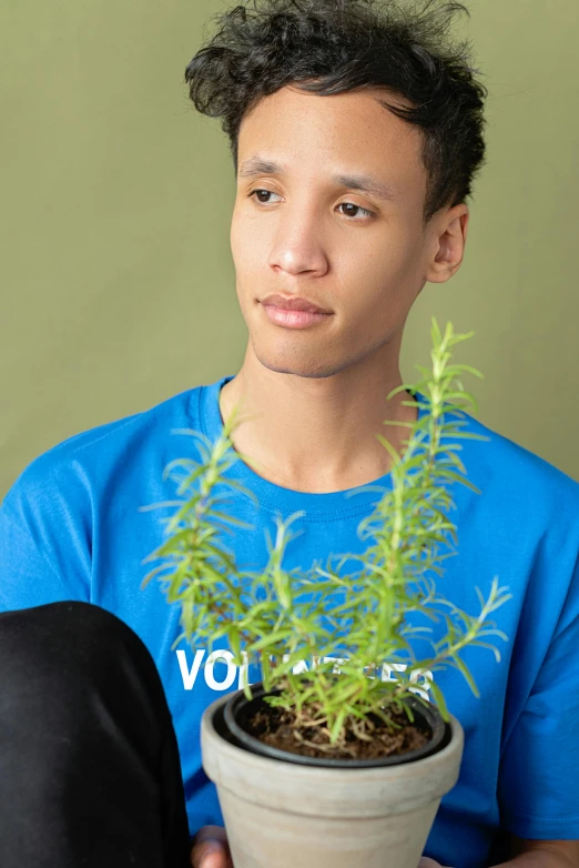 a young man is holding a potted plant, inspired by Jean Malouel, antipodeans, blue tight tshirt, 2022 photograph, profile image, dreadlock breed hair