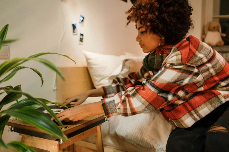 a woman sitting on a bed using a laptop computer, an album cover, trending on pexels, visual art, keyboardist, wearing a flannel shirt, gaming table, afro tech