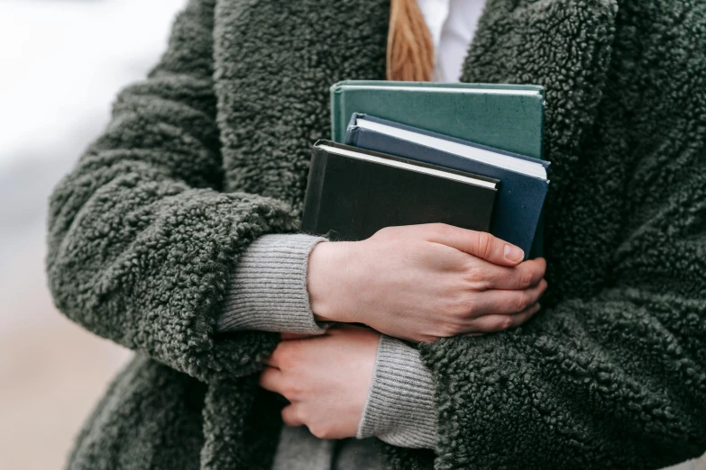 a close up of a person holding a book, cold, holding books, noelle stevenson, solid colours material