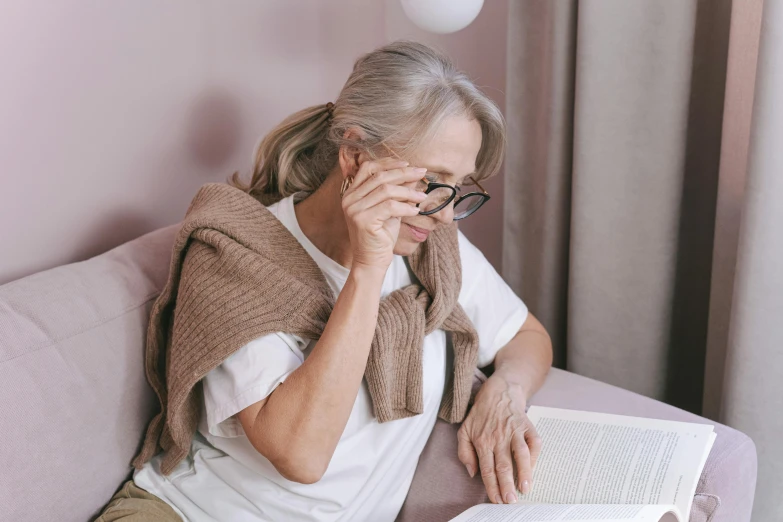 a woman sitting on a couch reading a book, trending on pexels, photorealism, wearing an eyepatch, elderly, health supporter, closes her eye
