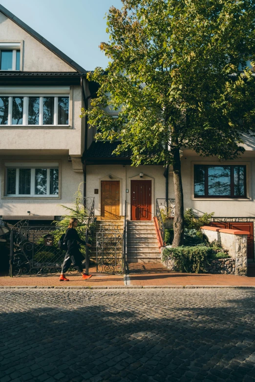 a person walking down the street in front of a house, by Tobias Stimmer, pexels contest winner, modernism, craftsman home, kreuzberg, terraced, lush surroundings