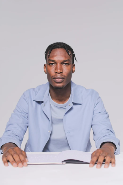 a man sitting at a table with a book, with brown skin, plain background, playboi carti portrait, emmanuel shiru