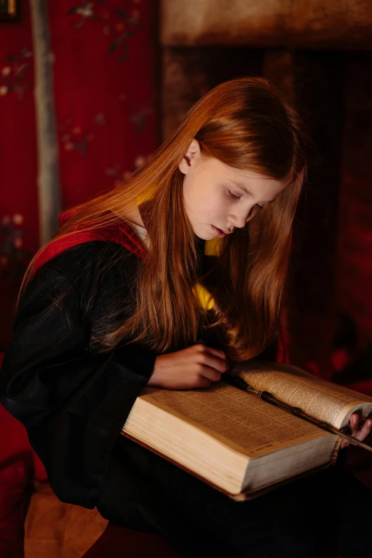 a young girl reading a book in front of a fireplace, inspired by Hermione Hammond, wearing red sorcerer's robes, studying in a brightly lit room, promo image, girl with brown hair