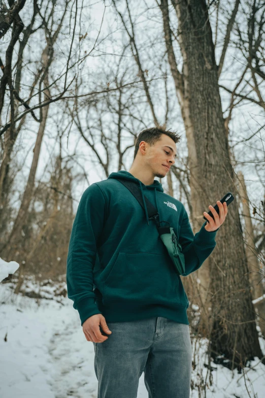 a man standing in the snow looking at his cell phone, trending on pexels, forest green, avatar image, wearing sweatshirt, dark photo