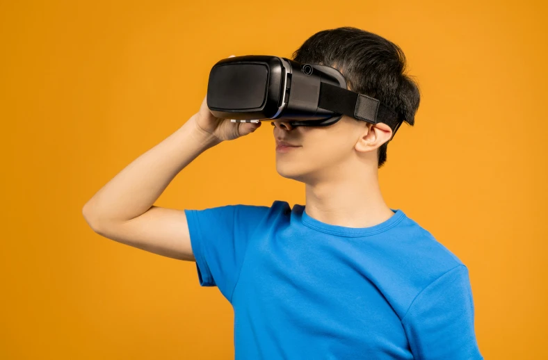 a boy in a blue shirt is using a virtual reality headset, an album cover, shutterstock, interactive art, in front of an orange background, wearing goggles, avatar image, 3 d modeling