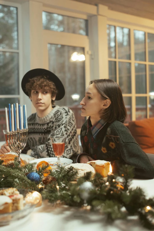 a group of people sitting around a table with food, on a candle holder, winter, beautiful jewish woman, older brother vibes