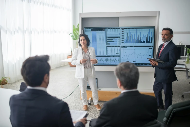 a group of people sitting around a table in a room, in front of a computer, graphs, performance, realistic »