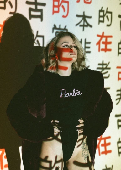 a woman standing in front of a wall with chinese writing on it, an album cover, inspired by Fei Danxu, trending on pexels, girl at a fashion show in hell, portrait of kim petras, patriotism, performing
