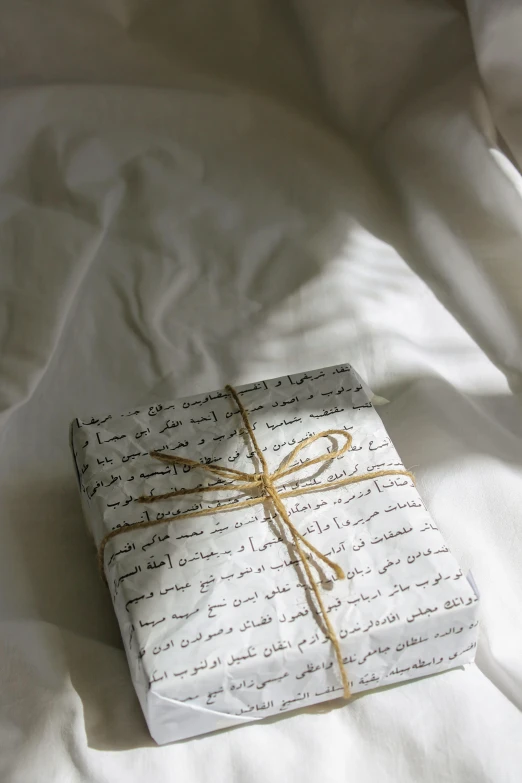 a wrapped gift sitting on top of a bed, by Alice Mason, pexels contest winner, hurufiyya, arabic calligraphy, wearing white pajamas, instagram story, taken in the late 2010s