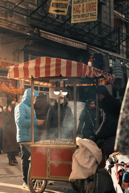 a man standing next to a cart filled with food, trending on unsplash, photorealism, busy streets filled with people, all face covered with a fire, wintertime, 8 k film still