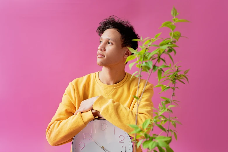 a man holding a clock next to a plant, an album cover, trending on pexels, pink clothes, nonbinary model, avatar image, thoughtful pose